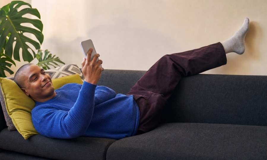 Pessoa relaxa no sofá enquanto olha para um celular